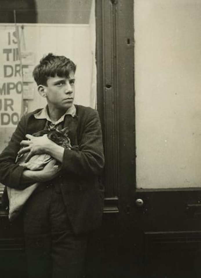 Garçon Avec Un Chat Dans Les Bras Appuyé Contre Une Vitrine by Dora Maar