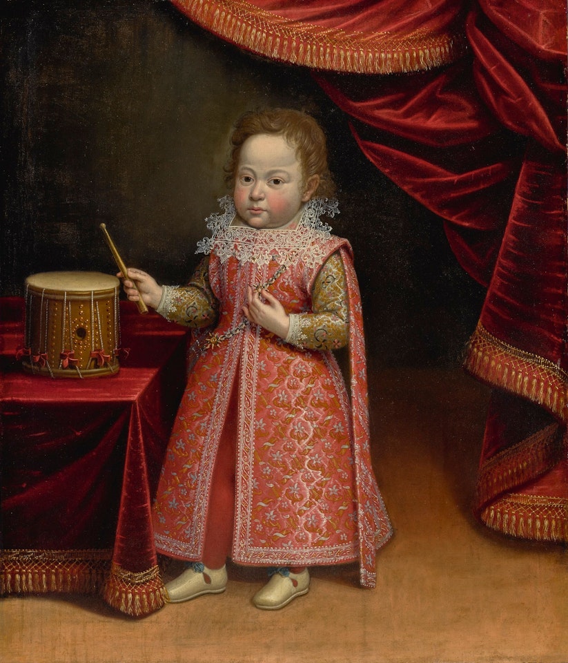 PORTRAIT OF A YOUNG BOY WEARING AN ELABORATE RED DRESS, STANDING NEAR A DRUM IN AN INTERIOR by Florentine School