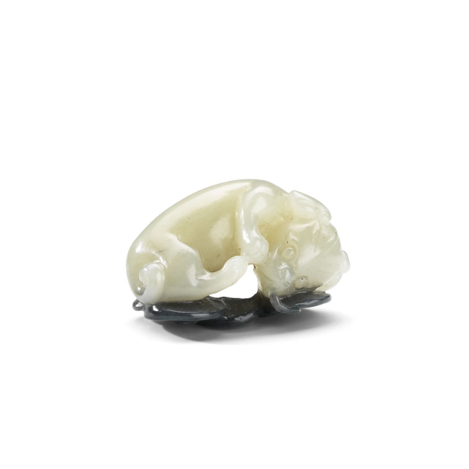 A BLACK AND WHITE JADE 'DOG AND COINS' CARVING by Anonymous