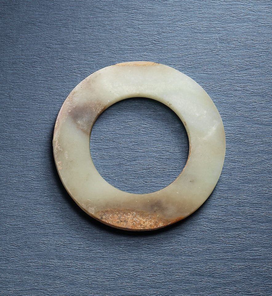 A GREENISH-WHITE AND RUSSET JADE RING, HUAN by Anonymous