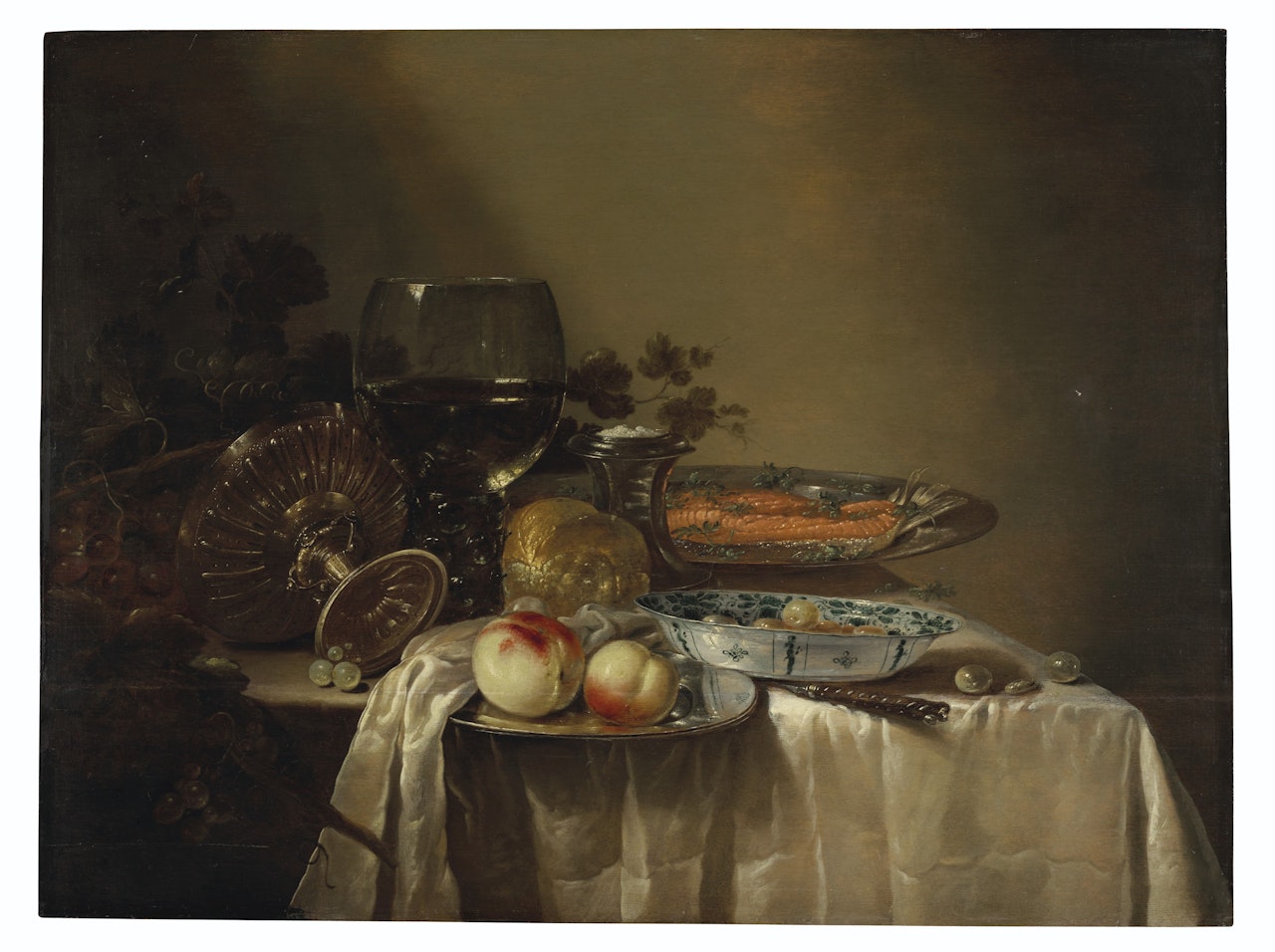 A roemer, an upturned tazza, grapes, peaches and salmon on pewter platters, olives in a porcelain bowl, and other objects on a partly draped table by Adriaen Jansz. Kraen