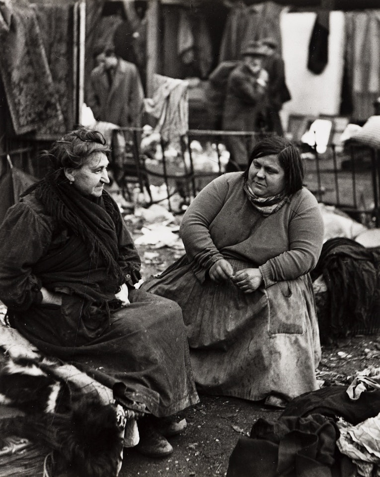 Two women talking in the flea market by André Kertész