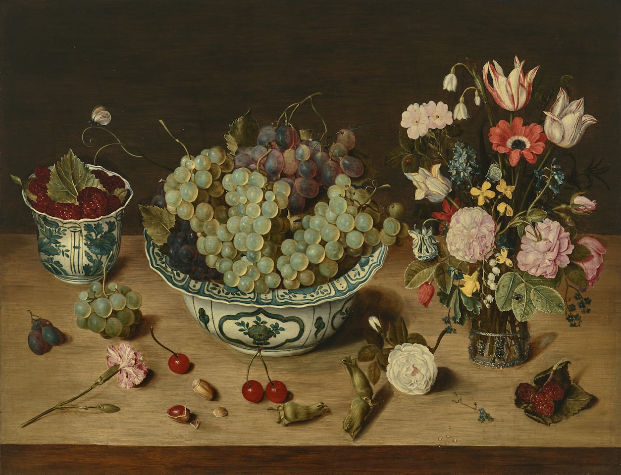 Grapes in a wan-li porcelain kraak , raspberries in a wan-li beaker, tulips, roses and other flowers in a glass vase, with scattered fruit, flowers, and hazelnuts on a ledge by Isaak Soreau
